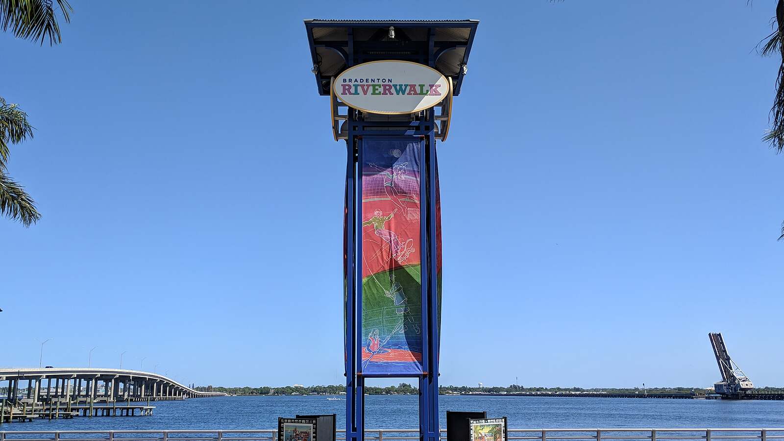 The Bradenton Riverwalk sign tower on the Manatee River, with the Green Bridge behind it.
