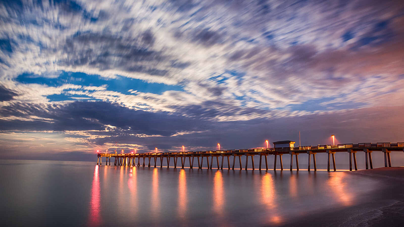 The Venice Fishing Pier at dusk, its lights reflected in the calm Gulf water.